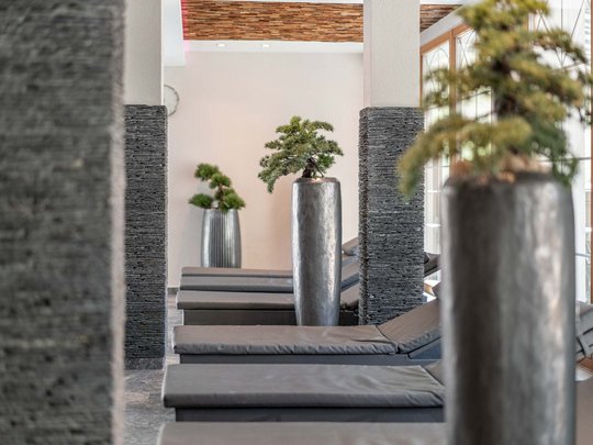 Saunadörfl und Bergsee in Ihrem Hotel in Tirol mit Pool Entspannungsbereich mit grauen Liegen und großen Pflanzgefäßen im Innenraum