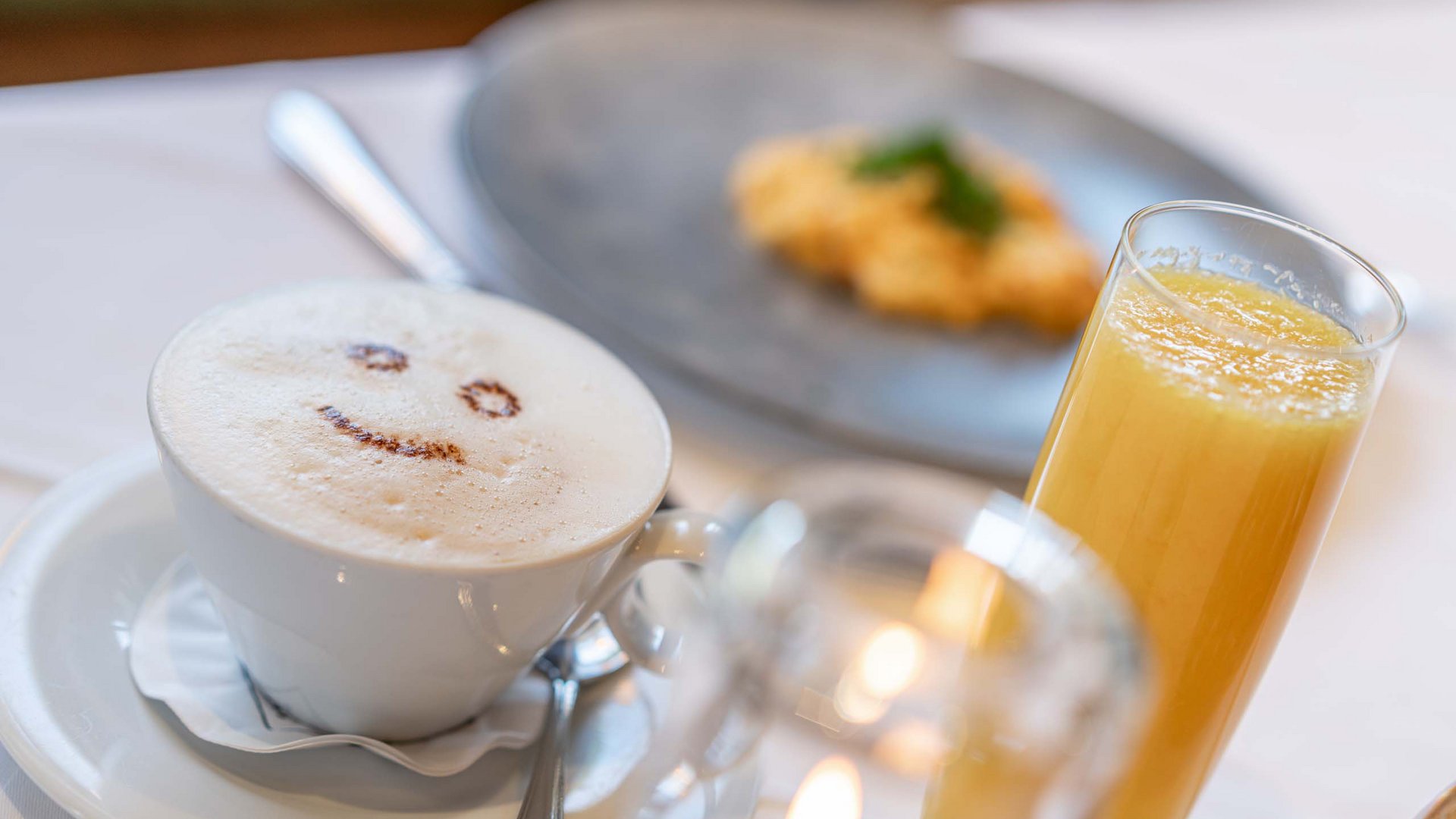 Morning indulgence in Vent: our accommodation with breakfast Coffee with smiling milk foam face, orange juice, and breakfast snack