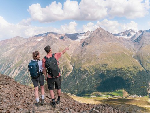 A summer holiday in Ötztal: a paradise for mountain lovers Two hikers with backpacks looking at a mountainous landscape with clouds