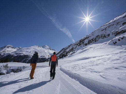 Winterwandern, Langlaufen und Rodeln in Vent Zwei Wanderer auf verschneiter Bergstraße bei sonnigem Himmel