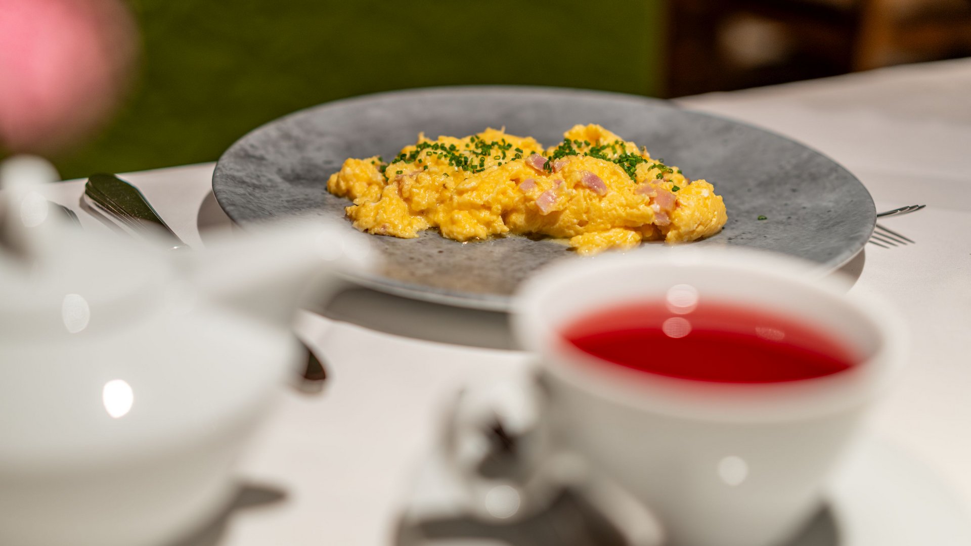 Morgendlicher Genuss in Vent: Ihre Unterkunft mit Frühstück Rührei mit Schinken und Schnittlauch auf grauem Teller, rote Getränke in Tasse