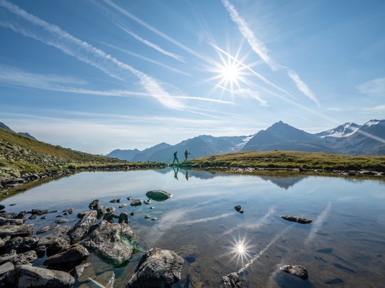 Wandern in den Ötztaler Alpen: von Ihrem Hotel in die Berge Wanderer am Bergsee bei sonnigem Himmel und reflektierenden Bergen