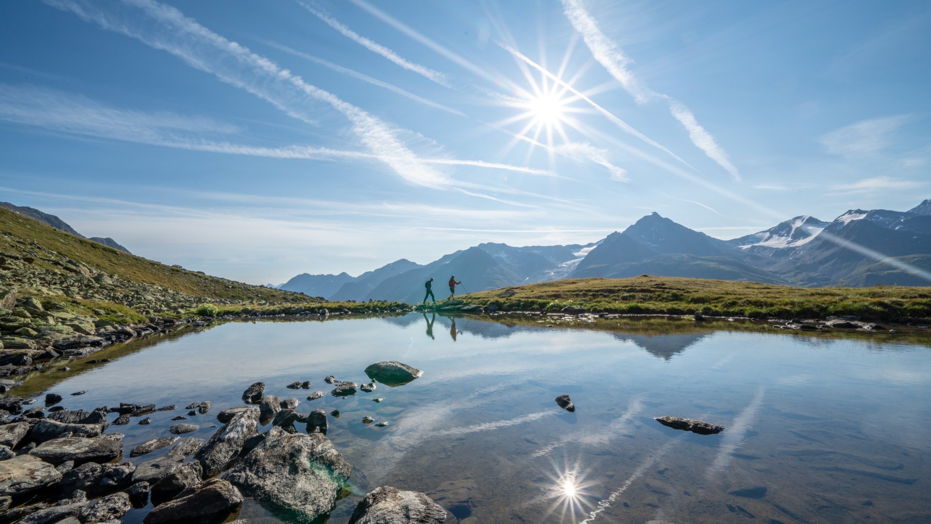 Wandern in den Ötztaler Alpen: von Ihrem Hotel in die Berge Wanderer am Bergsee bei sonnigem Himmel und reflektierenden Bergen