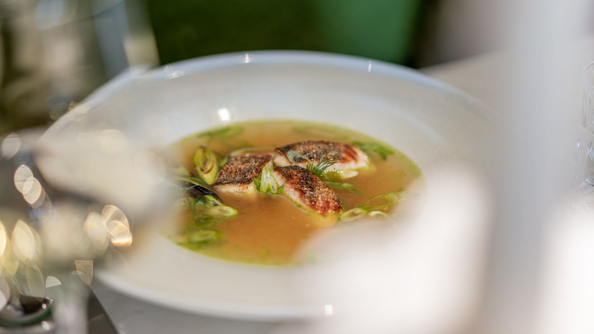 Natural indulgence at our restaurant in Vent Fish fillets in clear broth with spring onions in a white bowl