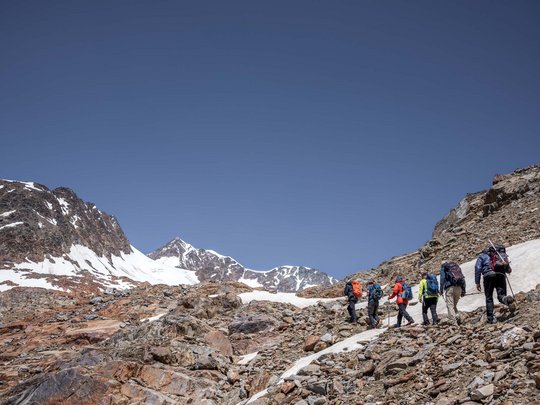 Sur le Similaun et la Wildspitze de notre hôtel à Vent Groupe de randonneurs gravissant un terrain rocheux dans les montagnes enneigées