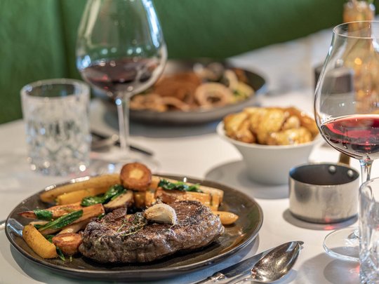The heights of indulgence in Vent: our restaurant, Die Post Steak with vegetables on plate and red wine in glass on a set dining table