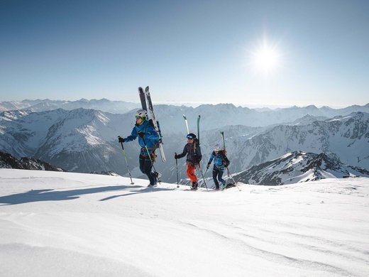 Backcountry skiing near Vent: start directly from our hotel Three skiers hiking up snowy mountains under bright sun
