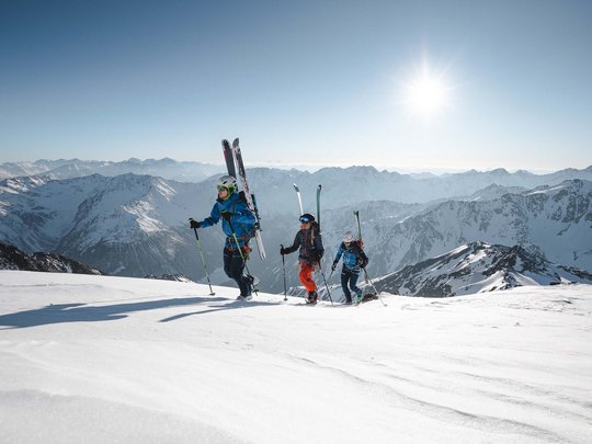 Backcountry skiing near Vent: start directly from our hotel Three skiers hiking up snowy mountains under bright sun