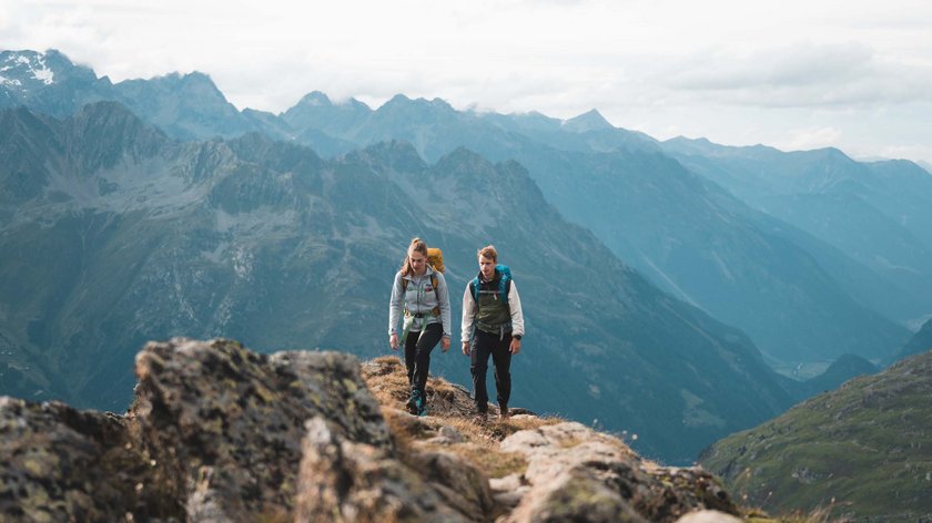 Der Ötztaler Urweg Zwei Wanderer mit Rucksäcken wandern in den Bergen bei bewölktem Himmel