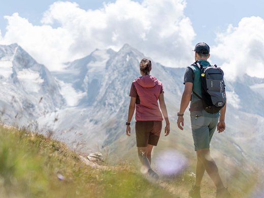 Die Inklusivleistungen in Ihrem Hotel im Ötztal mit Wellness Zwei Wanderer gehen auf Pfad vor schneebedeckten Bergen bei bewölktem Himmel