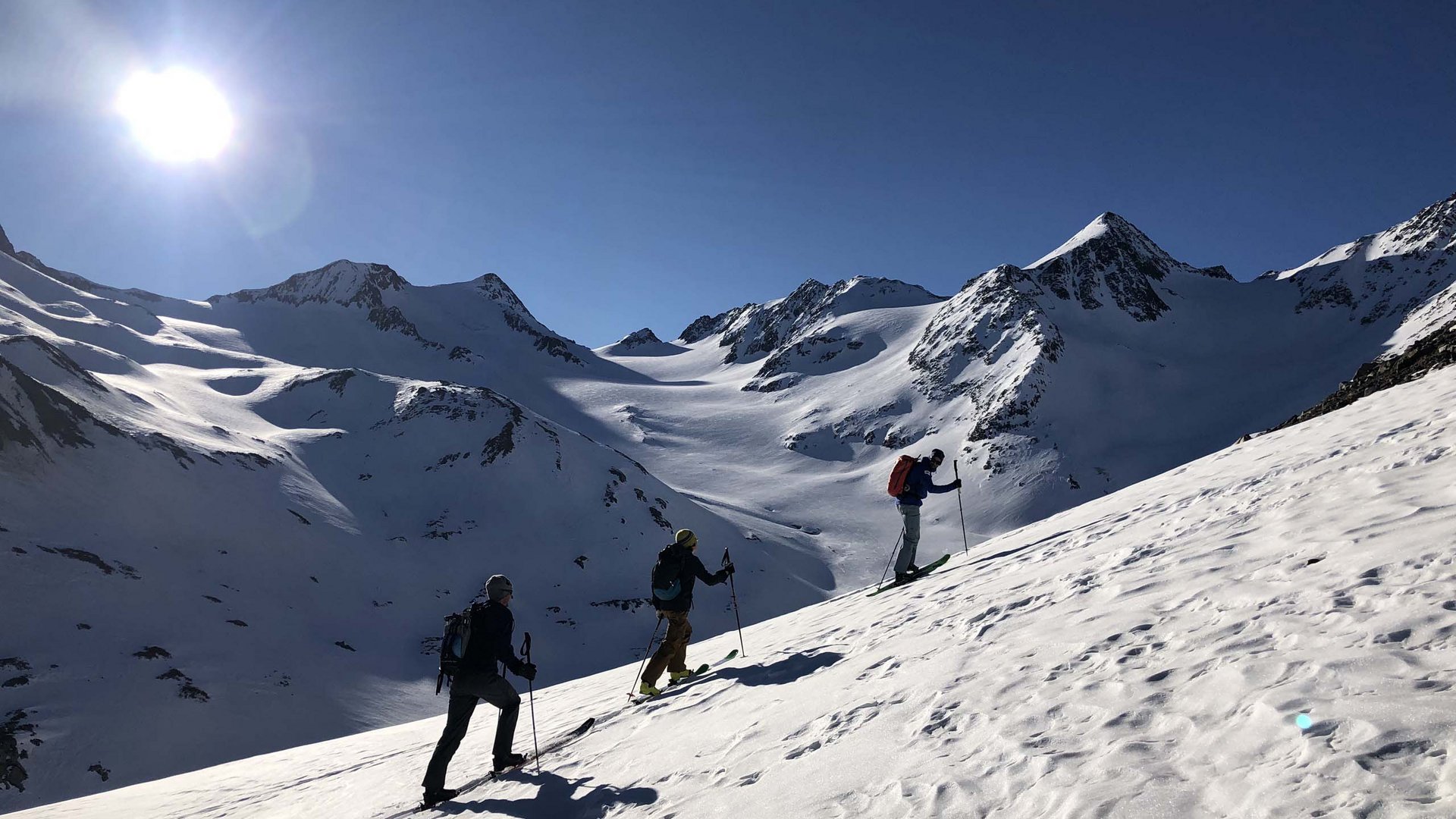 Backcountry skiing near Vent: start directly from our hotel Three ski tourers ascending a snowy mountain slope in sunny weather