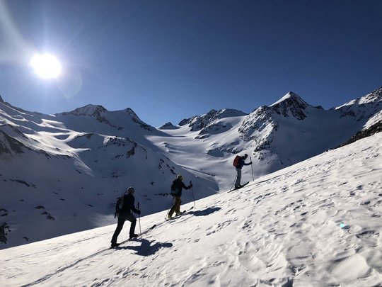 Backcountry skiing near Vent: start directly from our hotel Three ski tourers ascending a snowy mountain slope in sunny weather