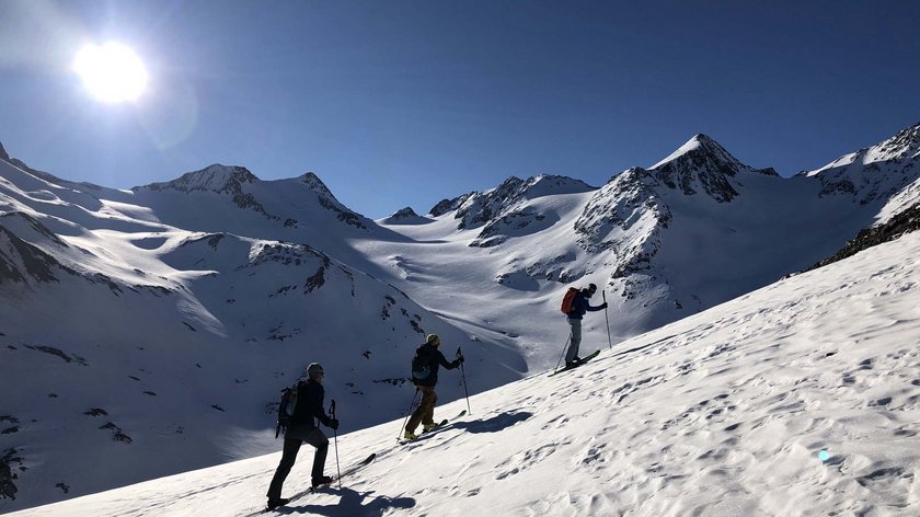 The chill of the slopes, the warmth of the pool Three ski tourers ascending a snowy mountain slope in sunny weather
