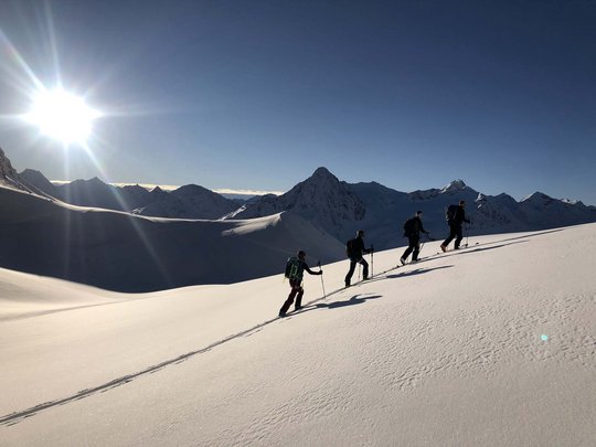 Backcountry skiing near Vent: start directly from our hotel Four ski tourers ascending snowy slope in bright sunlight