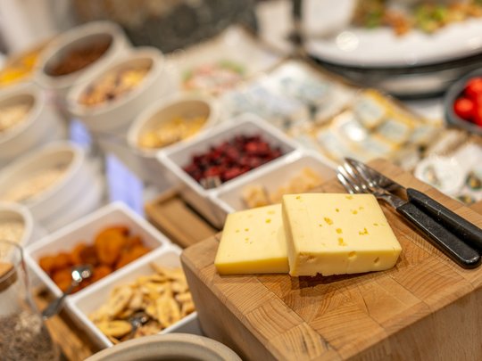 Morgendlicher Genuss in Vent: Ihre Unterkunft mit Frühstück Zwei Scheiben Käse auf Holzbrett mit Zutaten und Küchenutensilien im Hintergrund