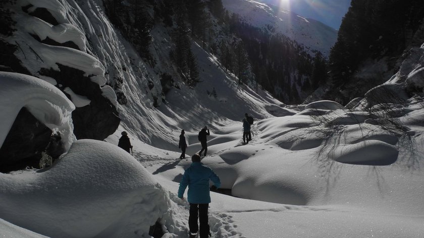 Zu Fuß durch den Winter Menschen wandern bei Sonnenschein durch verschneites Tal mit Bäumen