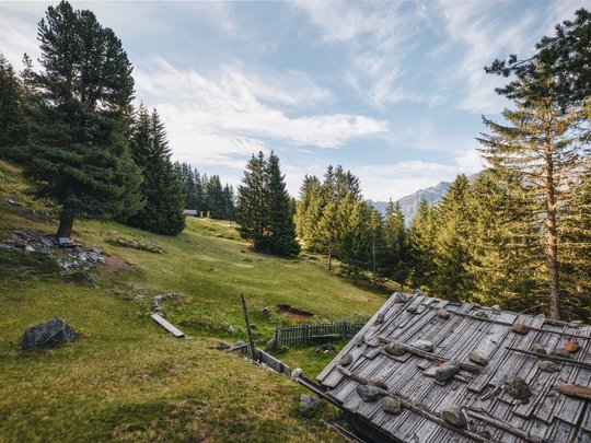 Wandern in den Ötztaler Alpen: von Ihrem Hotel in die Berge Berghütte mit steinigem Dach in grünem Tal und Nadelbäumen bei klarem Himmel