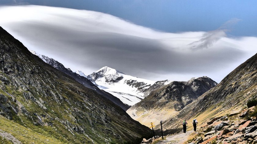 A magnificent high-altitude tour in the Ötztal Alps Hikers on mountain trail with snow-covered peaks and dramatic clouds
