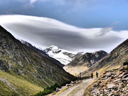 Alpinclub Similaun: durch die Liebe zum Berg vereint Wanderer auf Bergweg mit schneebedeckten Gipfeln und dramatischen Wolken