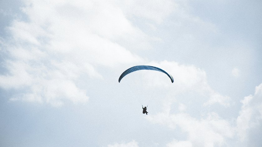 Paragliding, Canyoning und Rafting im Ötztal Person beim Gleitschirmfliegen vor bewölktem Himmel
