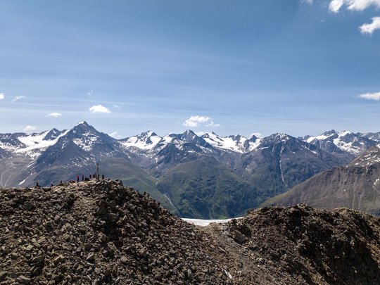 Sur le Similaun et la Wildspitze de notre hôtel à Vent Sommet rocheux avec randonneurs et Alpes enneigées en arrière-plan sous un ciel bleu