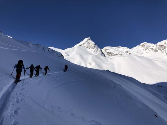 Backcountry skiing near Vent: start directly from our hotel Group of ski tourers on snowy mountain path under clear blue sky