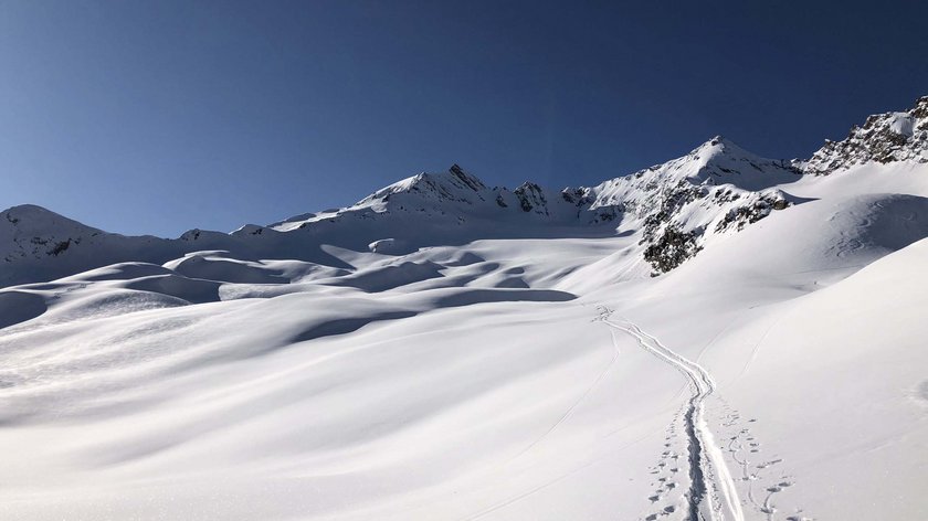 Skitour zu Saisonabschluss Schneebedeckte Berge unter klarem blauem Himmel mit Skispuren im Vordergrund