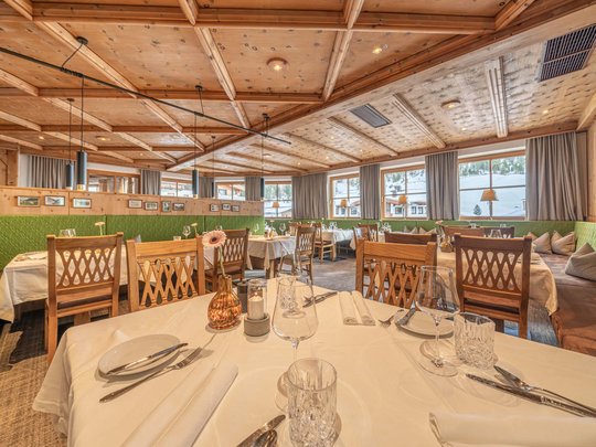The heights of indulgence in Vent: our restaurant, Die Post Cozy restaurant with wooden ceiling and set tables overlooking snowy landscape