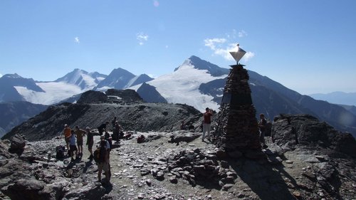 Sunrise tour with mountain breakfast Hikers on rocky mountain summit with glacier and summit marker under sunny sky
