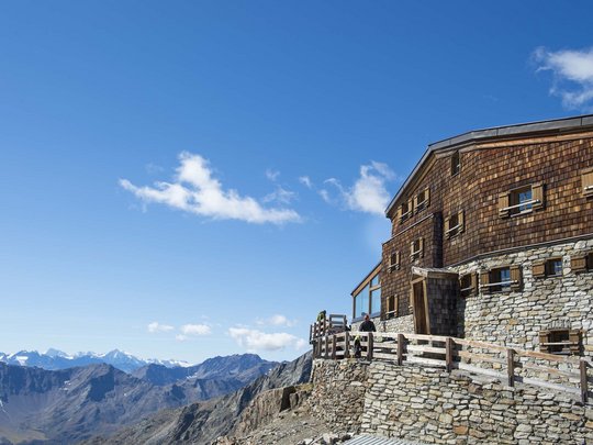 Alpinclub Similaun: durch die Liebe zum Berg vereint Bergütte aus Holz und Stein mit Blick auf alpine Berge unter blauem Himmel