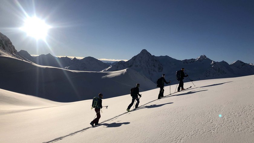 Vorteile einer Wanderführerin Vier Skitourengeher steigen bei Sonnenschein einen schneebedeckten Berg hinauf