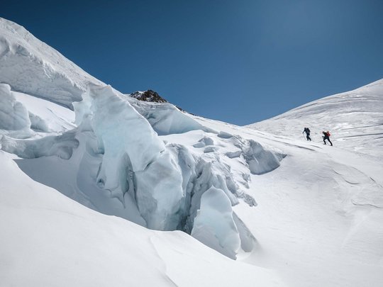 Backcountry skiing near Vent: start directly from our hotel Two skiers on snowy mountain with ice crevasses under clear blue sky