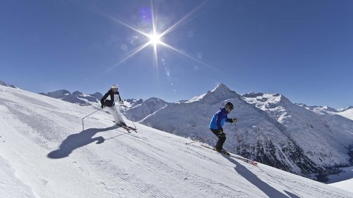 Your holiday in Vent: Enquire now with no obligation! Two skiers skiing down a snowy slope under a bright sunny sky