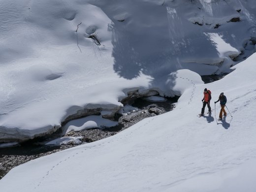 Spend a fantastic winter holiday in Tyrol. Two snowshoers walking beside a partially frozen stream in the snow