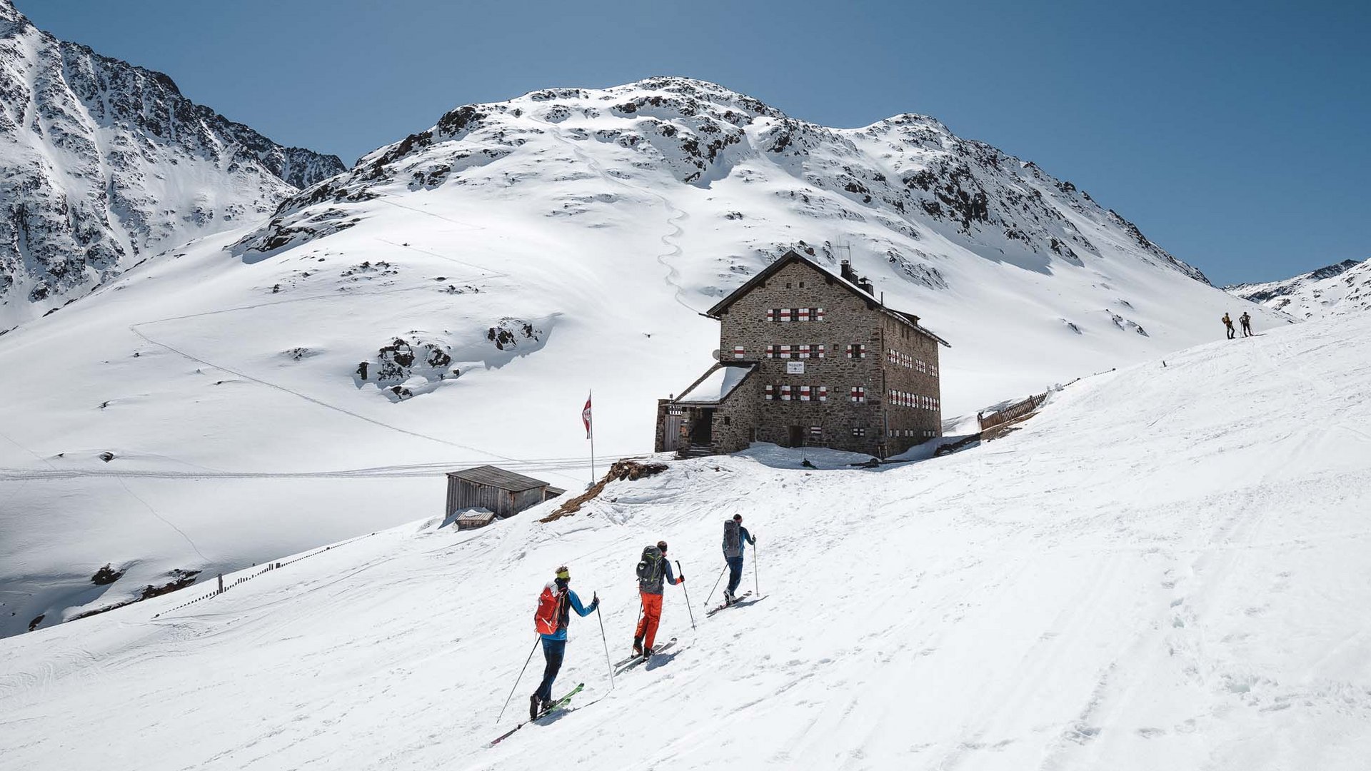 Backcountry skiing near Vent: start directly from our hotel Three skiers near a mountain hut in snowy alpine landscape under bright sun