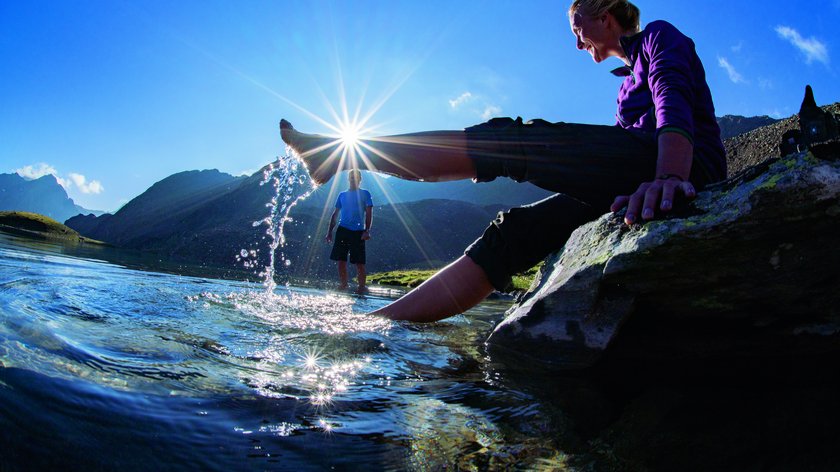 Brizzisee bei Vent: Tipp für Wanderer und Naturfreunde Frau sitzt am See, springt mit Fuß Wasser, Sonne glitzert am Bergsee
