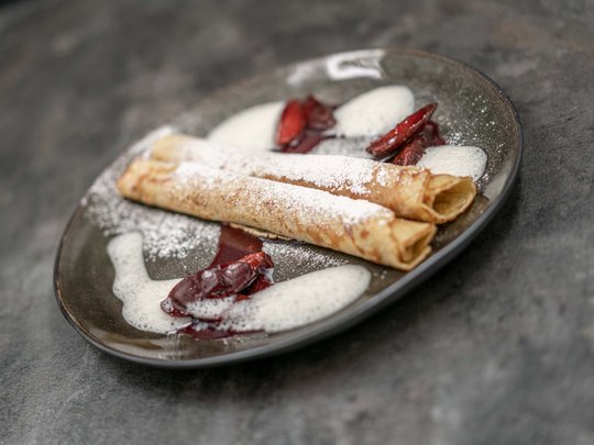 The heights of indulgence in Vent: our restaurant, Die Post Two crepes with powdered sugar, chocolate sauce, and foam on a dark plate