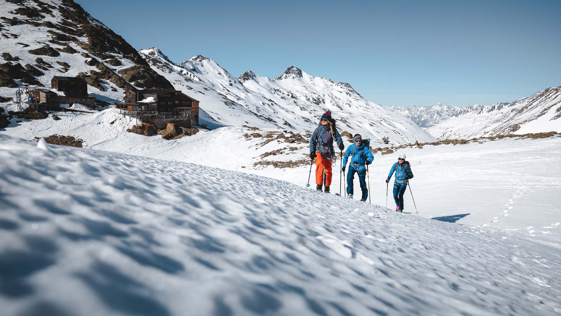 Natur- & Alpinhotel Post : téléchargements Trois randonneurs en tenue d'hiver marchant dans des montagnes enneigées sous un ciel clair