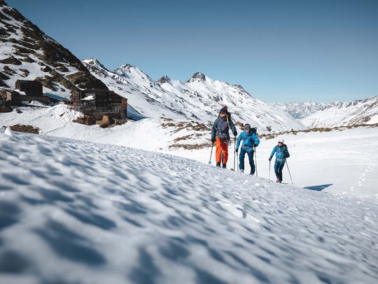 Backcountry skiing near Vent: start directly from our hotel Three hikers in winter gear trekking through snow-covered mountains under clear sky