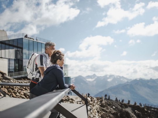 Natur- und Alpinhotel Post: Sehenswürdigkeiten im Ötztal Zwei Wanderer blicken von einer Terrasse auf Berglandschaft mit modernen Gebäuden