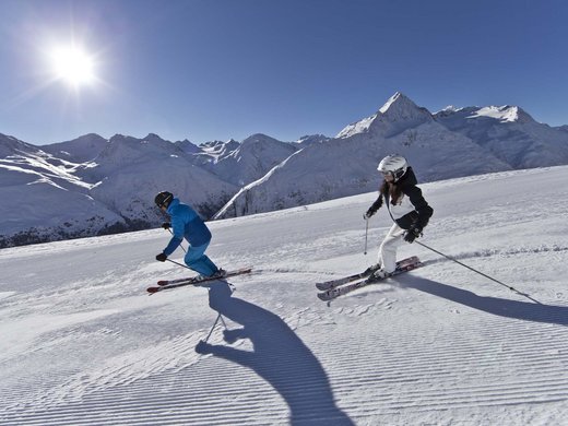 Spend a fantastic winter holiday in Tyrol. Two skiers skiing on a groomed slope under bright sun in the mountains