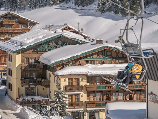 Lieu de rêve Vent : notre hôtel dans l’Ötztal Deux skieurs sur télésiège au-dessus de chalets enneigés