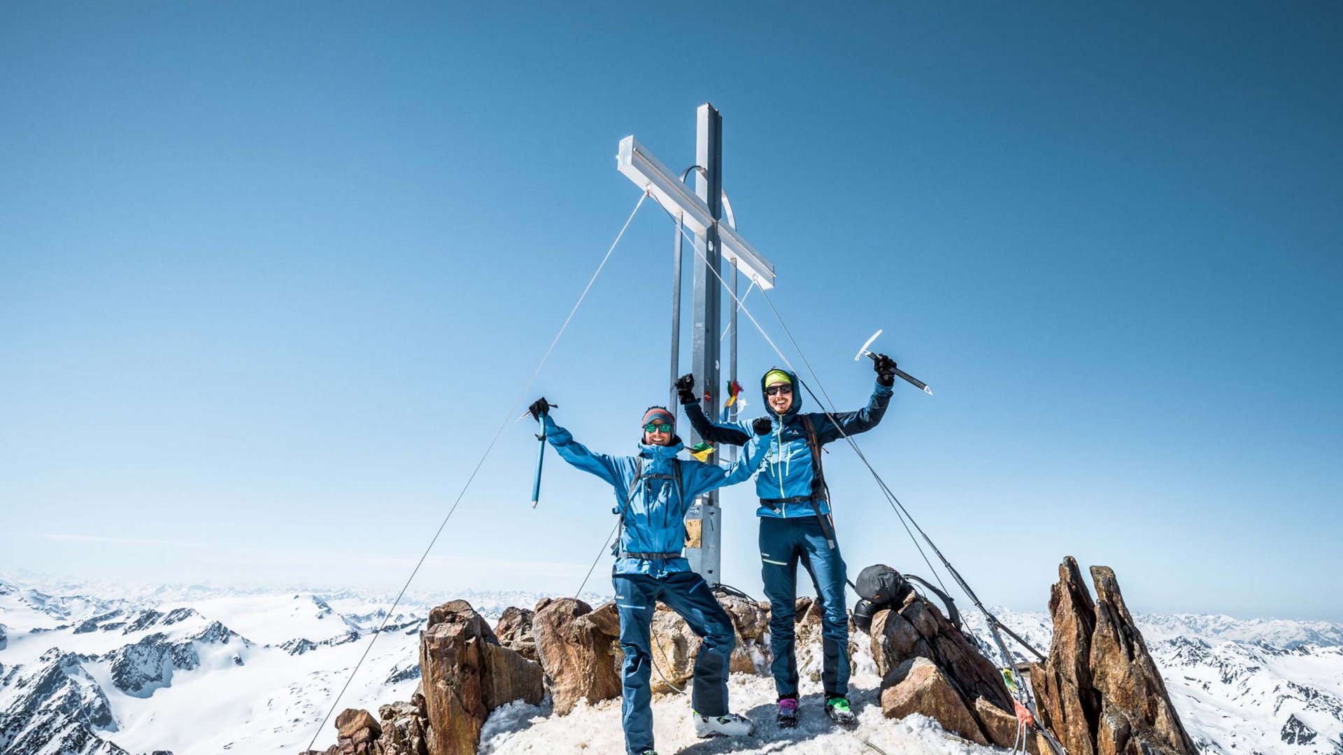 Alpinclub Similaun: durch die Liebe zum Berg vereint Zwei Bergsteiger feiern auf schneebedecktem Gipfel mit Kreuz bei klarem Himmel