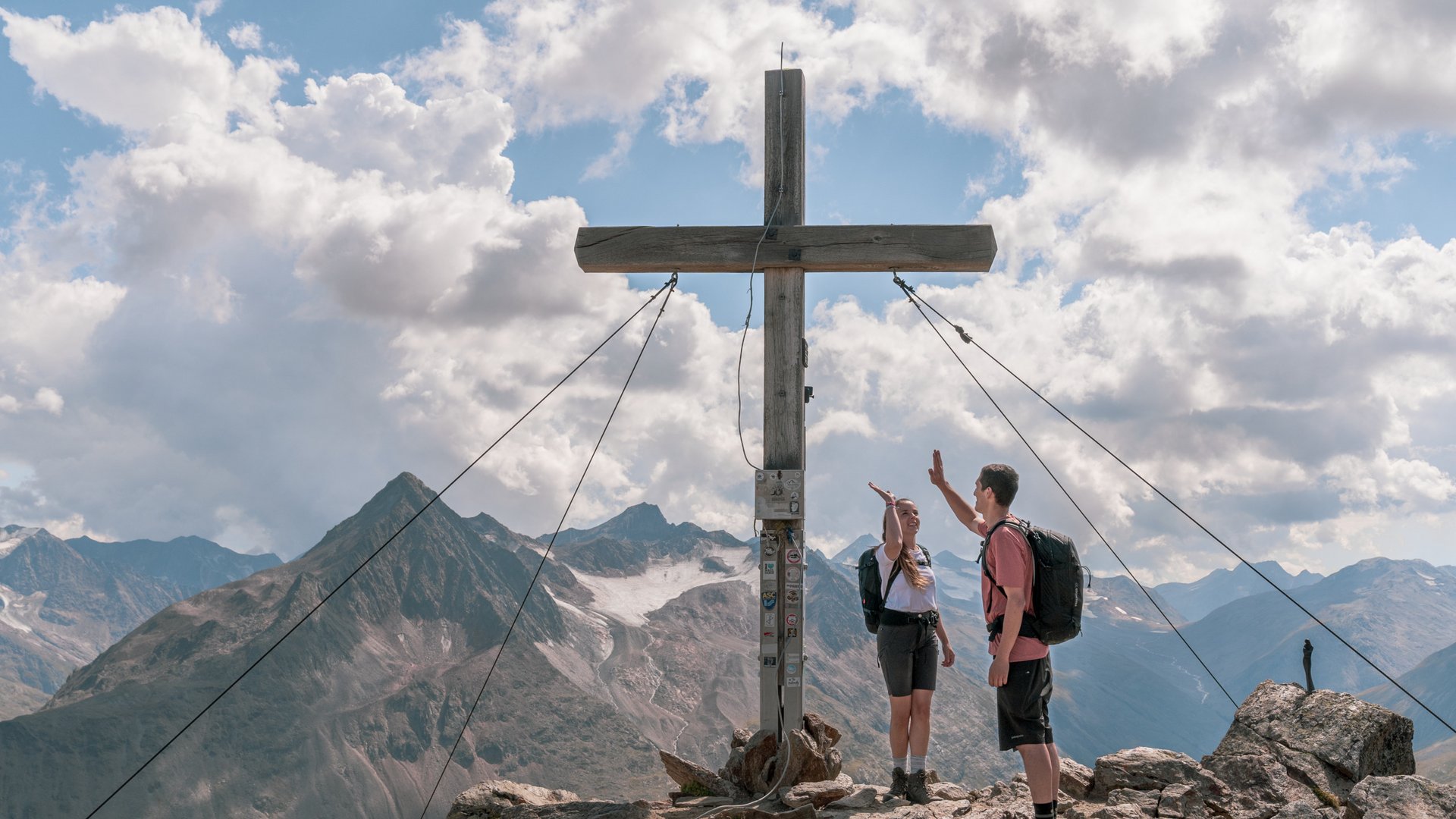 Sur le Similaun et la Wildspitze de notre hôtel à Vent Deux randonneurs font un high-five au sommet d'une montagne à côté d'une grande croix