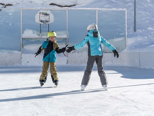 Winterwandern, Langlaufen und Rodeln in Vent Zwei Kinder mit Helmen beim Eislaufen auf einem Außenplatz im Schnee