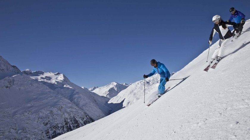 To-do-Liste für den Urlaub Drei Skifahrer fahren auf einem verschneiten Berg bei klarem Himmel