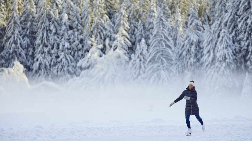 Vielfältige Wintererlebnisse Frau beim Schlittschuhlaufen vor verschneitem Wald an einem sonnigen Wintertag