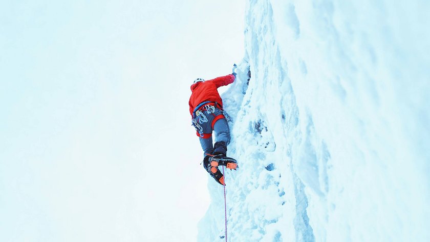 Winter climbing adventures in Vent Ice climber in red jacket ascending an icy cliff