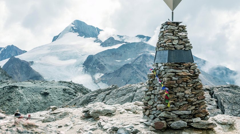 Explore Ötzi’s discovery site Stone memorial with snow-covered mountain and cloudy sky in background